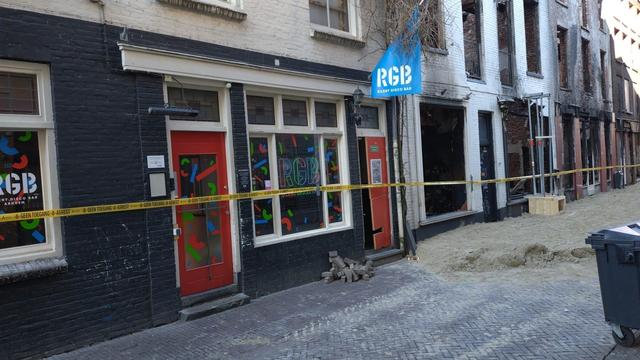 Het pand van The Move in Arnhem, ook getroffen door de brand in Arnhem. Zwarte gevel met lichte kozijnen. Rode deuren en een afzetlint wat waarschuwt voor asbest. Aan de gevel nog een vlag met RGB silent disco bar.