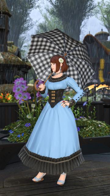 Esi posing with her left hand on her hip, and holding an umbrella against her right shoulder, wearing a long blue dress and a white flower on her hair. Rain falls all around her.