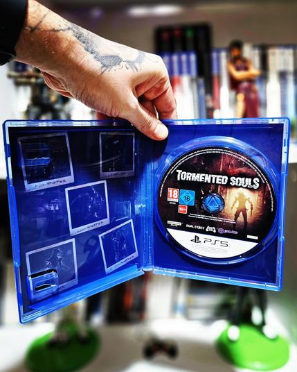 Imagen del interior de la caja con el disco de Tormented Souls en primer plano. La serigrafía del disco muestra un diseño oscuro con la silueta de la protagonista. De fondo, la ilustración del interior de la caja refuerza la atmósfera tétrica del juego.