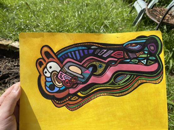 Picture of a drawing done in ink and marker. The artist is holding up the page in a grassy backyard. The drawing is of a shape with colorful negative space that is arranged in the rough form of some kind of sluggish creature with teddy bear ears. It is situated on a yellow backrgound.