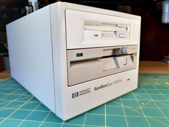 A Hewlett-Packard SureStoreTape 12000e, a very beige six-tape changer for data backup from the late 1990s. The tape drive and changer mechanism have been removed, replaced with a 3½" and a 5¼" floppy drive. Internally, they are connected to a GreaseWeazle, a device that connects over USB allowing the user to take very low-level flux backups of floppy disks.