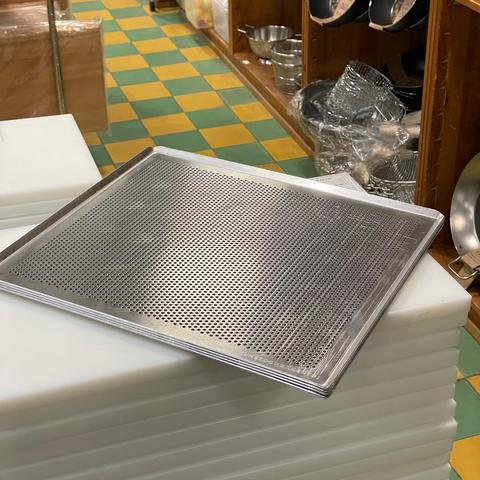 Foto af vores perforerede bageplade, stablet i en lille stak, oven på skærebrætter i Kunst og Køkkentøj-butikken i København.