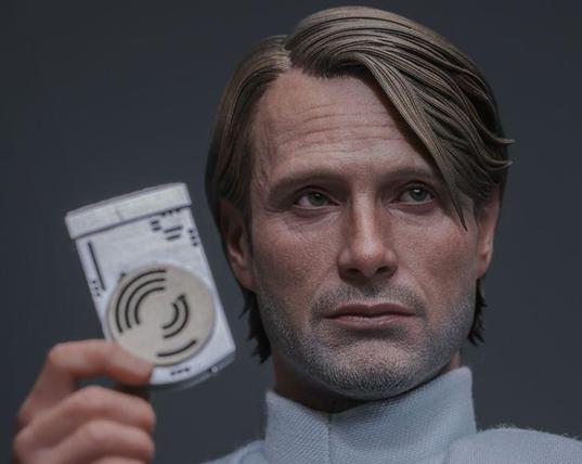 Photographie de la figurine resprésentant Galen Erso en tant que scientifique impérial. Il regarde vers la gauche de la photo (notre droite), tient dans sa main droite un support de données tel qu'aperçu dans #RogueOne, il porte son uniforme blanc.