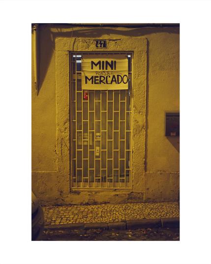 closed door of a tini supermarket with a paper sign saying „mini mercado ronja“ at night in a lisbon neighborhood