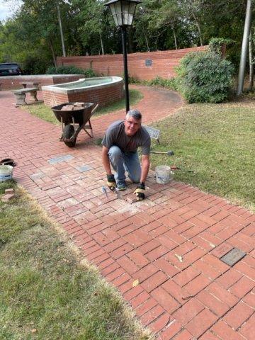 A photo of a man, kneeling, laying bricks for the pathway at the Hellen Keller Museum. 