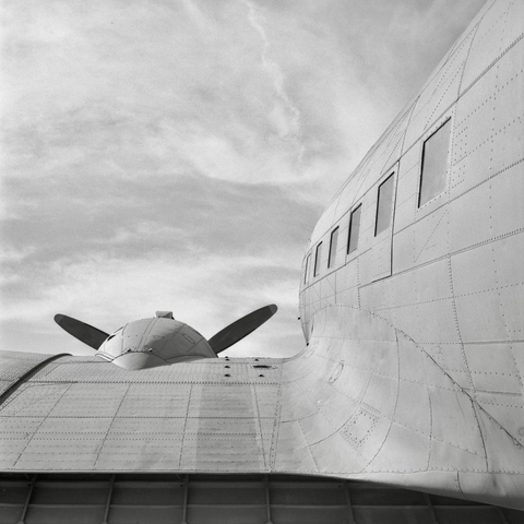 A black and white film photo. A view from behind the wing of a vintage Douglas C-47 Skytrain aircraft that is displayed outside of the Silent Wings Museum in Lubbock, Texas. Sunday, February 16, 2025. 