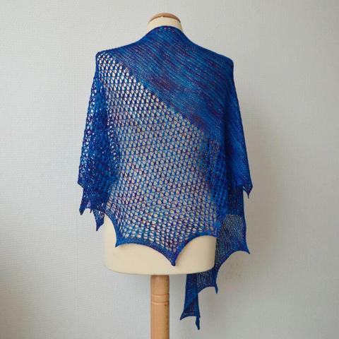 A knit shawl in blue variegated yarn, featuring both garter stitch and lace, shown from the back on a mannequin against a white background.