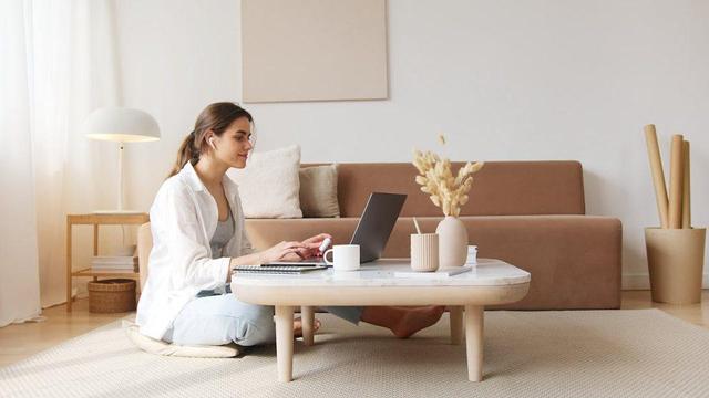 A woman seated on the floor, engaged with her laptop, surrounded by a comfortable and inviting atmosphere