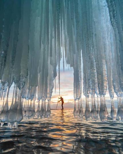 A man paddles through amazing ice formation on Lake Superior at sunrise.