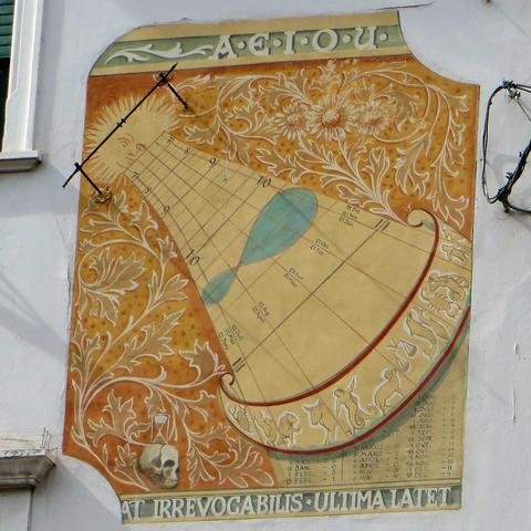 Wall with painted sundial. At the bottom a depiction of a skull and an hourglass, with a latin frase referring to the irreversible passing of time and the uncertainty of death. See also https://bestlatin.blogspot.com/2013/01/sundial-volat-irrevocabilis-ultima-latet.html