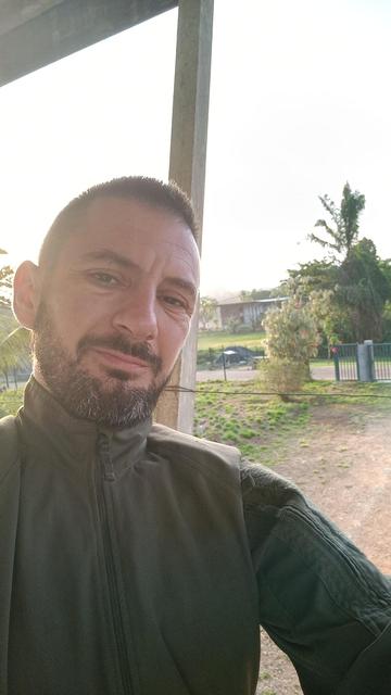 Dereck Carrillo en selfie, dans la commune de Maripasula en Guyane française. Tenue vert kaki, barbe courte, cheveu court brun, yeux marrons