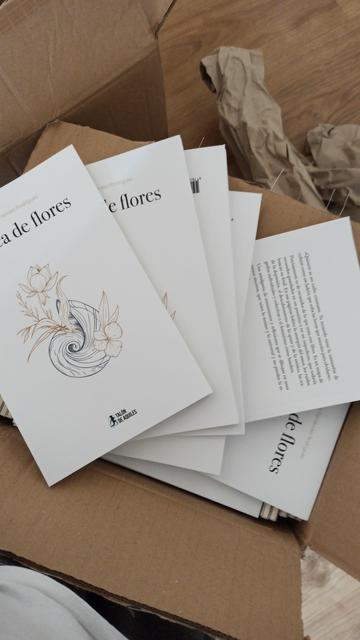 Foto de una caja con mis libros. Se llama marea de flores, en la portada hay una plantita que sale de una caracola sobre un fondo blanco