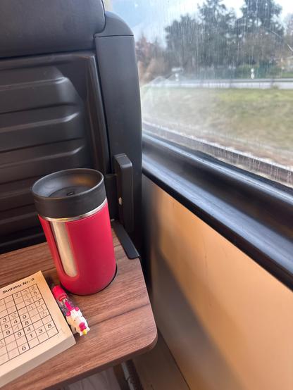 Blick aus zugfenster, links sieht man einen Thermokaffeebecher und einen Teil eines Sudoku-Heftes 