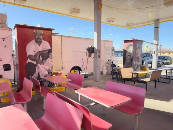 Photograph of an outside dining area attached to a taco truck. There are no customers. 
