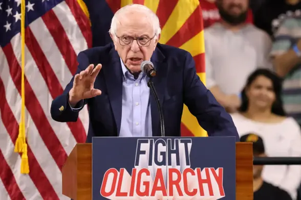 Bernie Sanders speaking at a rally where he appeared alongside the New York representative Alexandria Ocasio-Cortez. The sign says FIGHT OLIGARCHY.