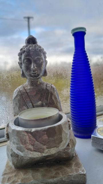 Buddha candle holder in front of blue bottle in a window/ Buddha Kerzenhalter vor einer blauen Flasche in einem Fenster
