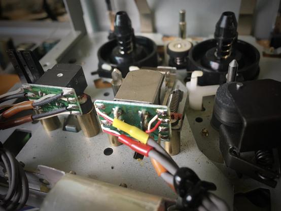 The upper side of the tape mechanism in a Tascam 464 multitrack cassette machine, as viewed from below the heads. The wires connecting to the erase head and record/playback head are visible, as well as the reels, idler tire and pinch roller assembly.