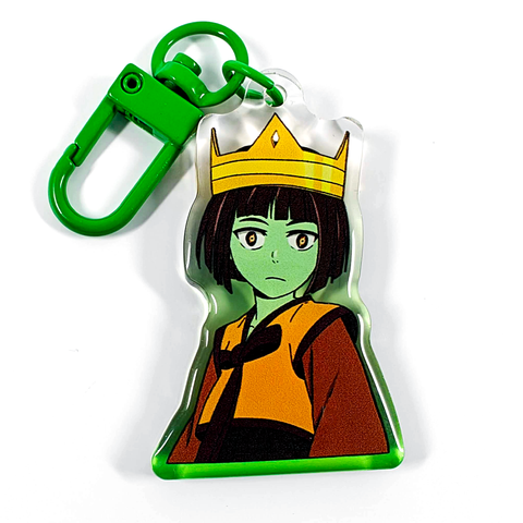 A picture of an acrylic keychain of Anaak from Tower of God. She looks shocked, wearing a gold crown and her classic outfit. The rim of the keychain is a gradient going from green at the bottom to clear at the top. It has a bright green clasp.
