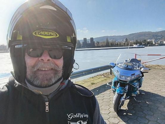 Ein alter Mann mit Sturzhelm und Sonnenbrille, dahinter ein Motorrad und die Mosel.