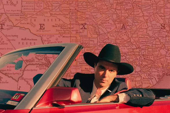 David Byrne in True Stories looking out from behind the steering wheel of a red convertible Chrysler LeBaron and sporting a black felt cowboy hat. 

Getty Images/Photo Illustration by Gwen Howerton