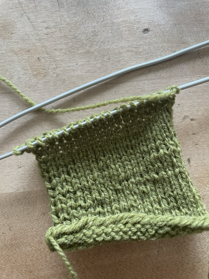 Gestrickte Maschenprobe aus grüner Wolle auf Holztisch