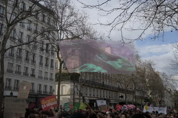 Protesters holding signs above their head and flying a massive, pink-ish transparent flag in a Paris street.