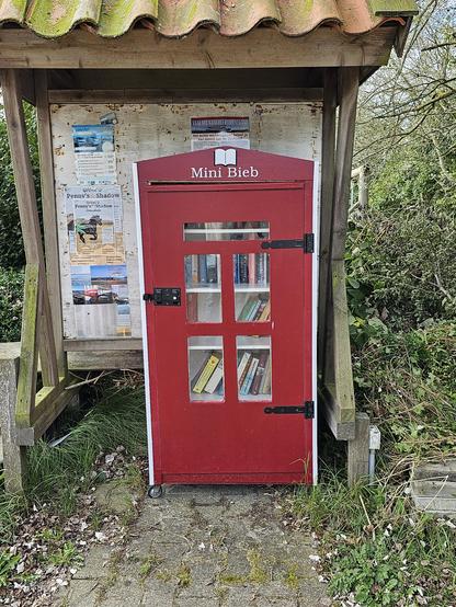 Ein roter öffentlicher Bücherschrank vor einem Touristen-Informationsstand mit der Aufschrift "Mini Bieb"