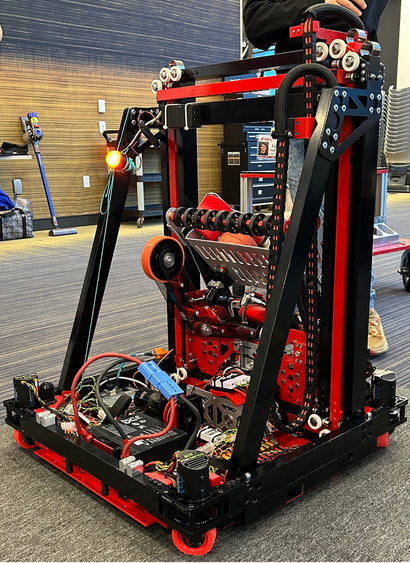 Black and red robot with a square base, vertical and diagonal structures, with wheels, pulleys, wires, connectors and other parts visible. A cropped person behind the robot gives a sense of scale, about 75cm x 75cm x 1m tall.