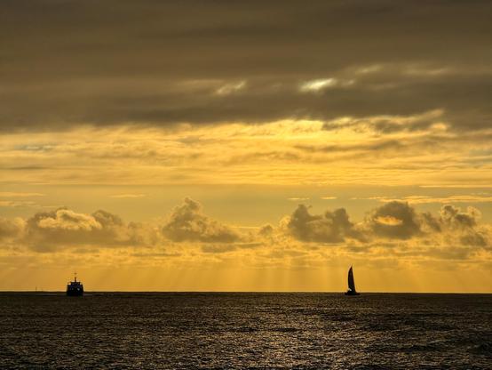 View of the sea at sunset, a ferry on the left and a sailboat on the right are drifting towards the horizon.