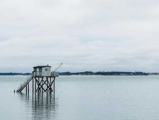 A fishing hut on stilts is located on the left, facing a calm and peaceful, oil-like sea of a blue-green hue.