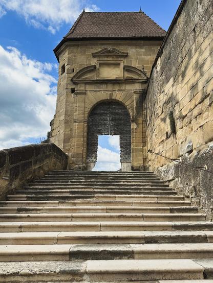 An ancient staircase leads to an equally ancient door. The door is open. The door frame reveals a blue sky and clouds.