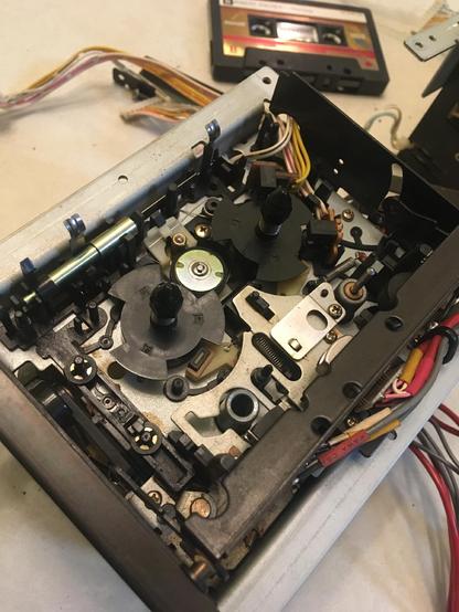 A close-up of the tape mechanism from an Akai MG614 multitrack cassette recorder, with a cassette tape in the background. The reels and idler tire of the mechanism are visible.