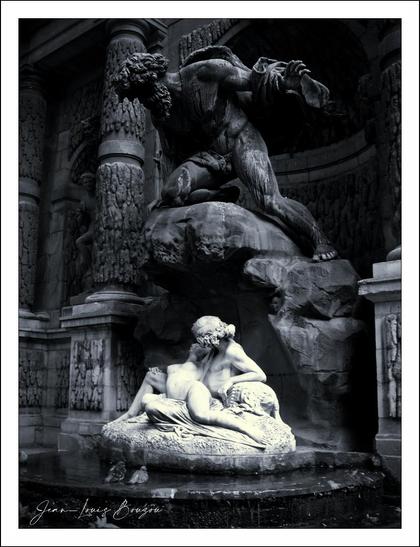 This image features a striking sculpture that captures a dramatic moment. At the top, a muscular figure, likely representing a powerful deity or force, looms with an imposing presence. His robust stance and intense posture suggest an act of strength or defiance, perhaps conveying themes of struggle or triumph.
Below him, another figure reclines gracefully in a more serene pose. This contrast creates a rich narrative tension between strength and vulnerability. The figure appears to be cradling a smaller form, enhancing the sense of protection or nurturing amidst turmoil.
The textures of the sculptures add to the depth of the piece, showcasing intricate details that evoke a sense of realism despite the stylized representations. The monochromatic palette invests the image with a timeless quality, allowing viewers to focus on the emotional weight and dynamics of the scene without the distraction of color.
Overall, the interplay of the figures could suggest a story of conflict, love, or coexistence, inviting contemplation on the duality of human experience. The viewer might reflect on the balance between power and tenderness, evoking a rich tapestry of interpretations based on individual perceptions and emotions.