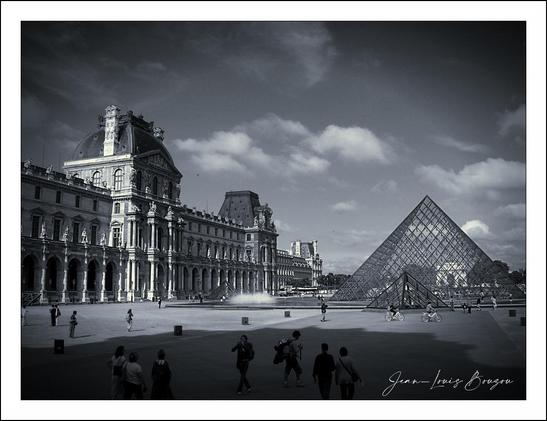 The image captures a striking contrast between the historic grandeur of the Louvre Museum and the contemporary elegance of the glass pyramid designed by I.M. Pei. On the left, the classical architecture of the museum stands with its ornate detailing and majestic facade, embodying centuries of art and culture. The pyramid, on the right, offers a sharp but harmonious juxtaposition, its sleek lines and transparent surfaces reflecting modernity.
The scene is alive with activity, as visitors wander around the courtyard, perhaps captivated by the rich history that surrounds them. The monochromatic palette adds a timeless quality, evoking a sense of nostalgia while emphasizing the architectural dialogue between the old and the new. This interaction invites contemplation about the evolution of art and architecture, highlighting how both can coexist and enhance one another. The image can evoke feelings of curiosity and appreciation for both past and present, urging viewers to explore and perhaps reflect on their own experiences within such iconic spaces.