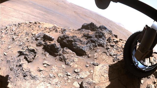 An image captured by the right front hazard avoidance camera of the Mars rover Perseverance, featuring a rocky mound and a wheel of the rover, with a Martian landscape in the background. 