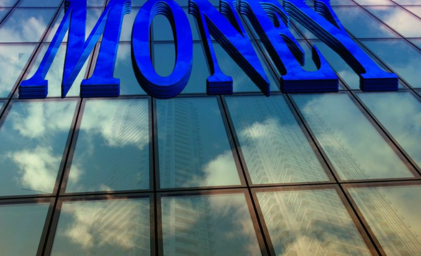 A large money sign displayed on the facade of a modern glass building, symbolizing finance and investment.