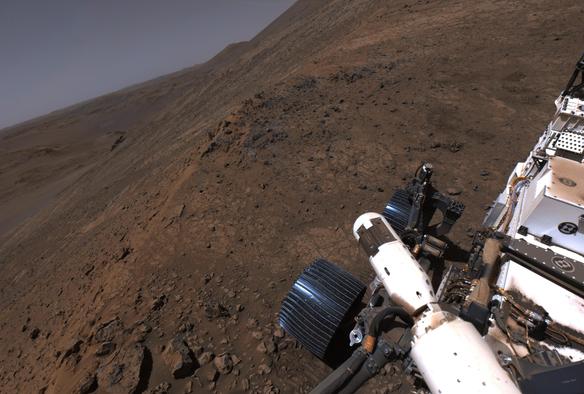 A shot captured by Mars rover Perseverance with her left navigation camera. Percy stands on the steep slope of a rocky mound, itself sitting on the steep slopes of the rim of Jezero Crater.