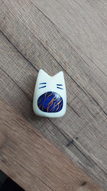 Un nouveau gardien du sommeil est terminé. c'est une petite figurine en forme de chat stylisé avec un motif rond bleu sombre sur le ventre, avec des marbrures dorées et des Moustaches bleues