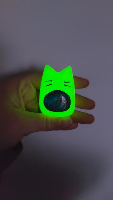 Le gardien au ventre bleu et marbrures dorées, brille doucement d'une lumière verte fluo dans une pièce plus sombre.
