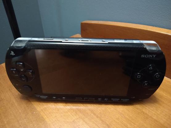 My black PSP 1000 seated in a corner of my room on a wooden surface