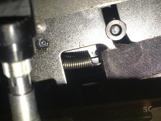 A close-up, shadowy side view of the tape mechanism from an Akai MG614. A spring grips the newly installed paperclip attached to the (unseen in his photo) Slide Eject plastic.