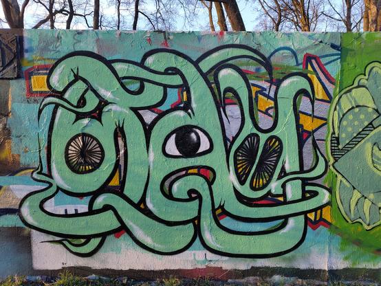 A graffiti on a wall, with 3 letters S,A,Y, written in green like twisted tentacles, with an eye in the hole of the A