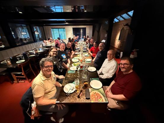 Photo of a dinner party with a long table. About 22 people sitting and looking into the camera.