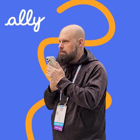  Sam from The Blind Life stands outside a convention center, holding up his phone while using the Ally app.