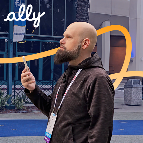Sam from The Blind Life looks upward while interacting with the Ally app on his phone, against a blue background with orange curves.