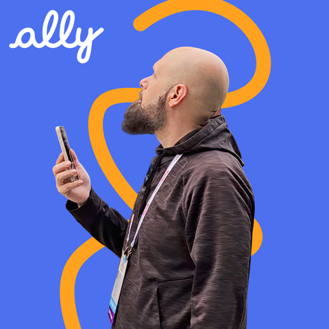 Sam from The Blind Life holds his phone close while using the Ally app, focused and engaged, in front of a blue background with orange curves.