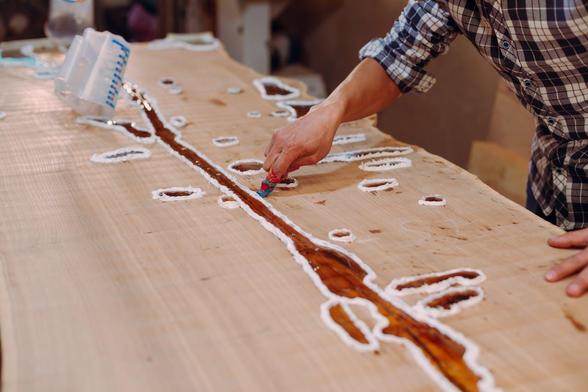 A man carefully painting a table with a brush, showcasing his attention to detail in a bright workspace