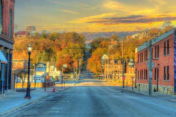 A quiet street stretches towards a hill covered in vibrant autumn foliage