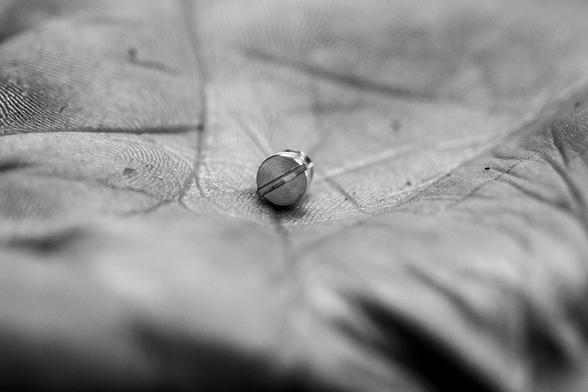 Macro black and white photo of a small screw held in the palm of a slightly dirty, greasy hand.
