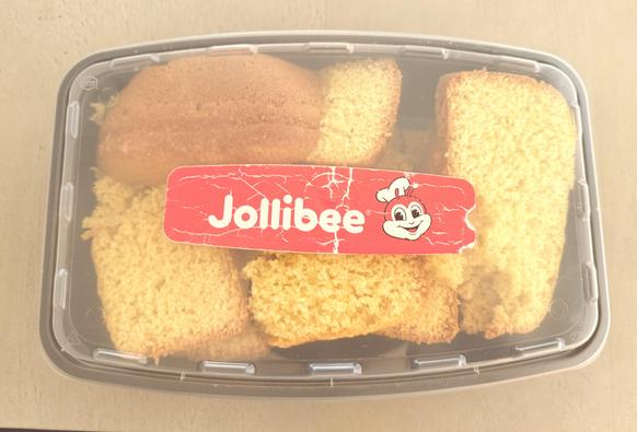 Cornbread in a black plastic food container with a clear lid. The lid is labeled “Jollibee”.